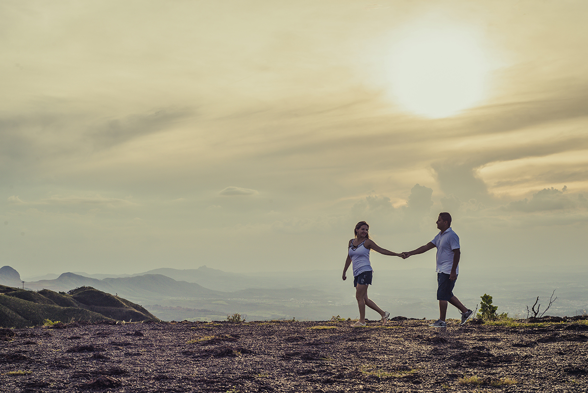 Casal caminhando de mãos dadas em um ensaio pré wedding na serra do Rola Moça MG com uma linda vista da montanha e do pôr do sol