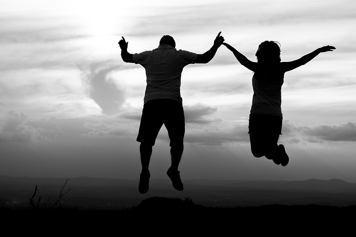 Casal feliz pulando juntos em uma foto de silhueta com uma linda vista da Serra do Rola Moça BH no click do fotografo de casamentos em Belo horizonte BH MG