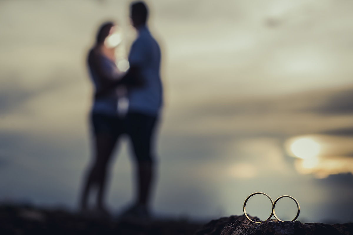 Foto de Alianças juntas com o casal se abraçando no fundo em ensaio pre wedding feito na serra do Rola Moça MG