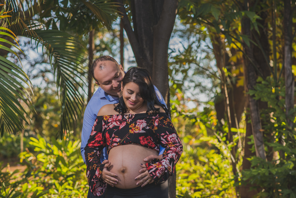 Casal abraçado olhando para a barriga da grávida no ensaio de gestante feito no parque municipal jacques cousteau 