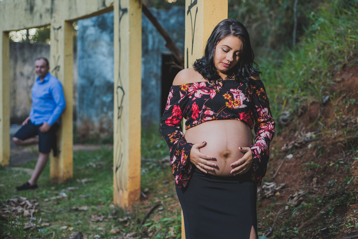 mamãe segurando a barriga com o pai ao fundo no ensaio de gestante feito no  no parque municipal jacques cousteau feito pelo fotógrafo João Paulo em belo horizonte