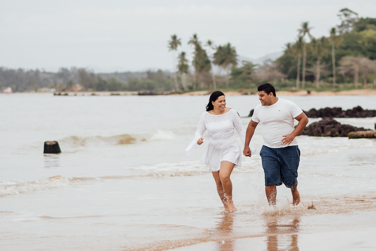 noivos correndo de mãos dadas na praia no ensaio pre wedding feito em coqueiral de aracuz -es