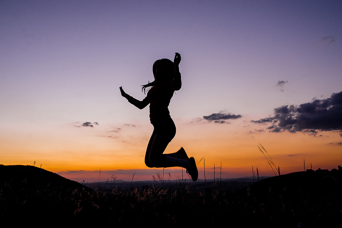 garota pulando feliz no book de 15 anos em belo horizonte com o pôr do sol ao fundo na linha de trem do belvedere