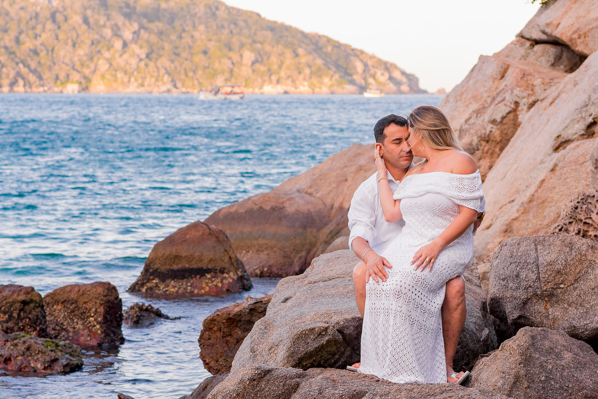 Noiva sentada no colo do noivo sentado nas pedras no pre wedding em arraial do cabo