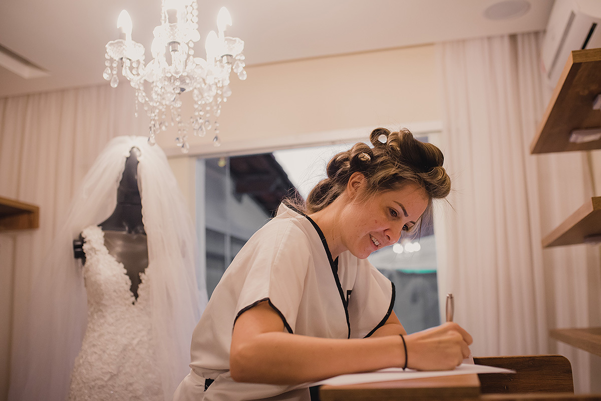 noiva escrevendo os votos com o vestido de noiva ao fundo no dia da noiva em bh