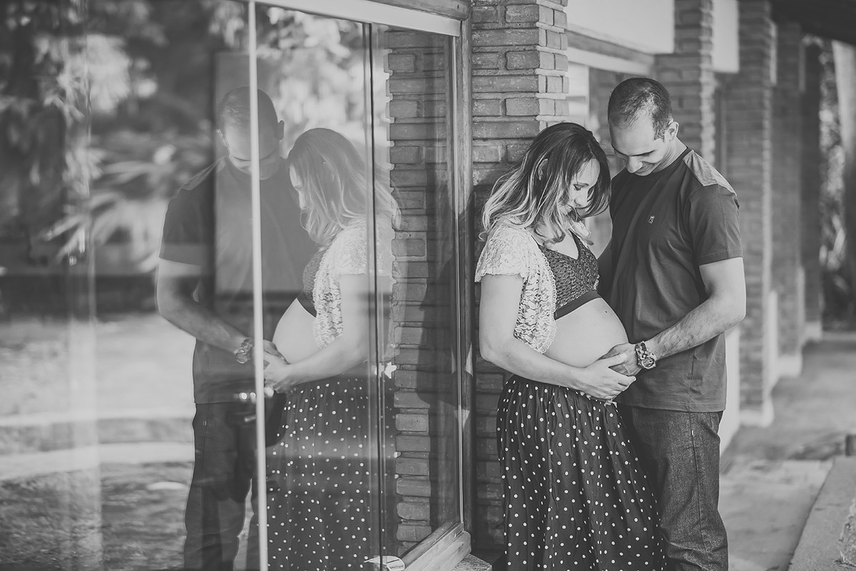 Grávida e pai olhando para a barriga da gestante junto com reflexo no vidro