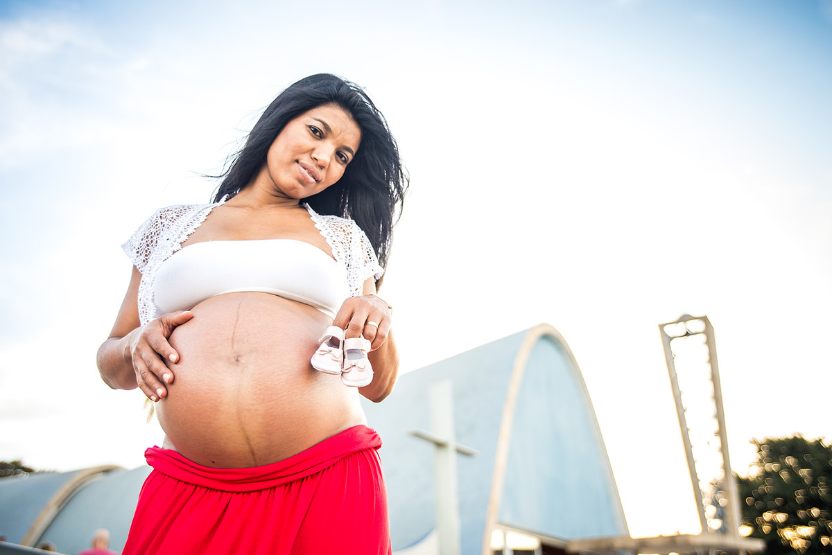 gestante em frente a igrejinha da Pampulha segurando o sapatinho de bebê