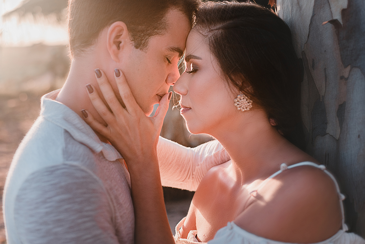 Ensaio_précasamento_Renata_e_Otávio_Ceará-Mirim_Rio_Grande_do_Norte_14_10_2019 Close de casal abraçado, com as testas encostadas. Ambos um de frente para o outro. A moça acaricia o rosto do rapaz e passa o polegar em sua boca, enquanto a luz do sol invade