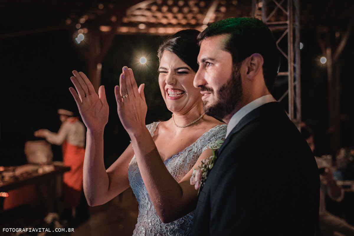 Fazenda Real III - Macaíba - RN - A noiva e o noivo estão assistindo homenagens feitas para eles durante a recepção. A noiva está aplaudindo e sorrindo.
