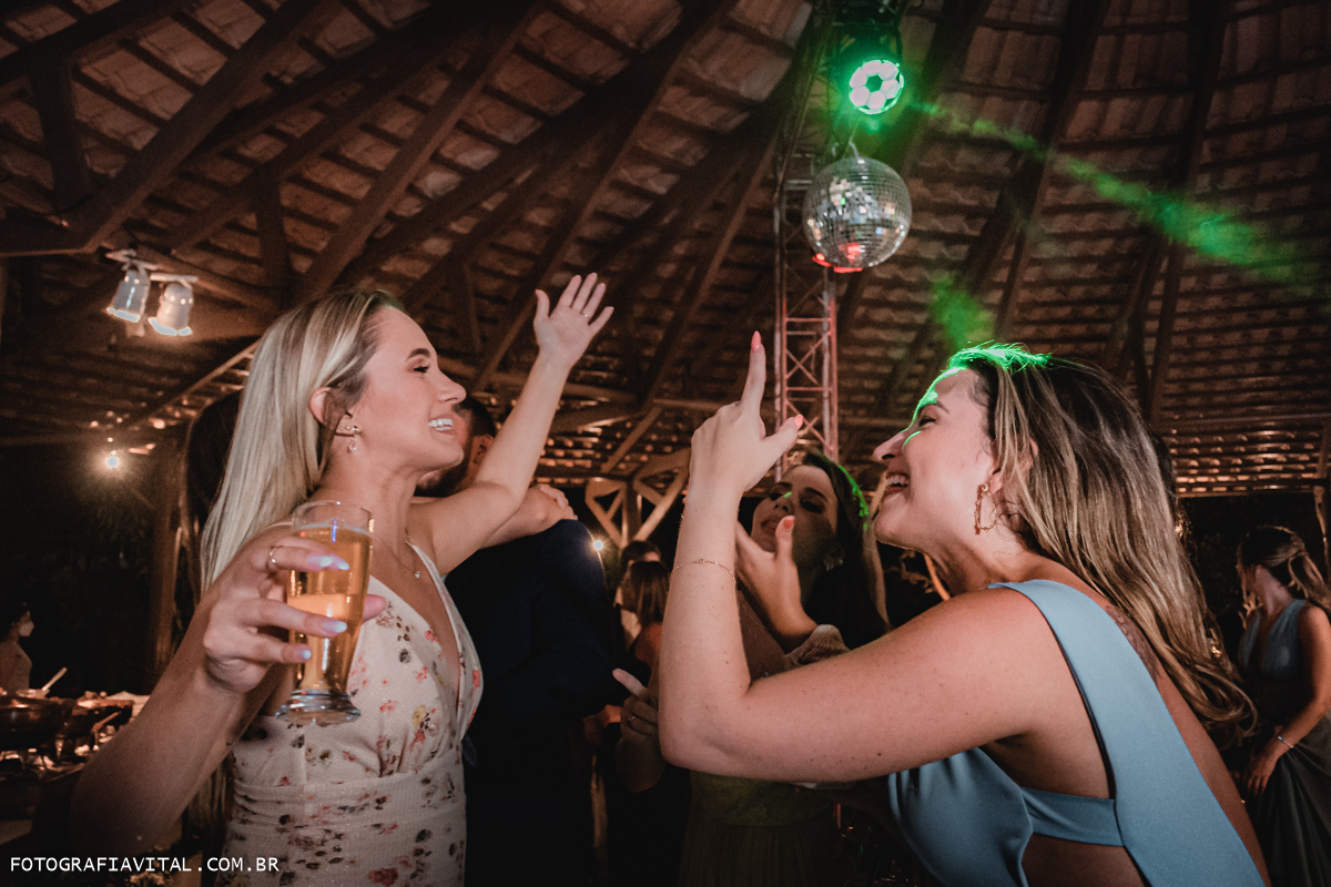 Fazenda Real III - Macaíba - RN - Duas convidadas cantando e apontando para o teto. Elas estão rodeadas de luzes coloridas e seguram copos de bebidas alcóolicas.