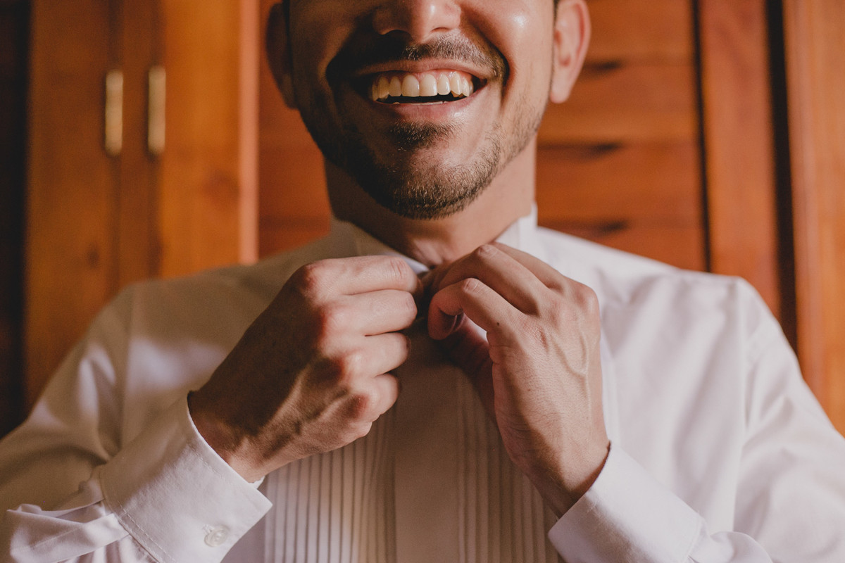 noivo sorrindo enquanto arruma a camisa do casamento