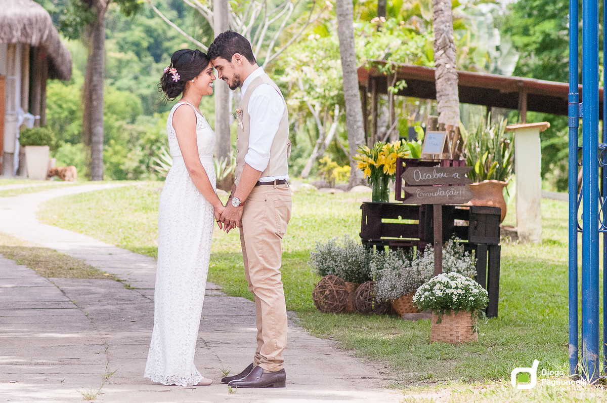 Noivos apaixonado se olhando no caminho da fazenda com jarros de flores ao fundo. Foto Diogo Pagnoncelli.