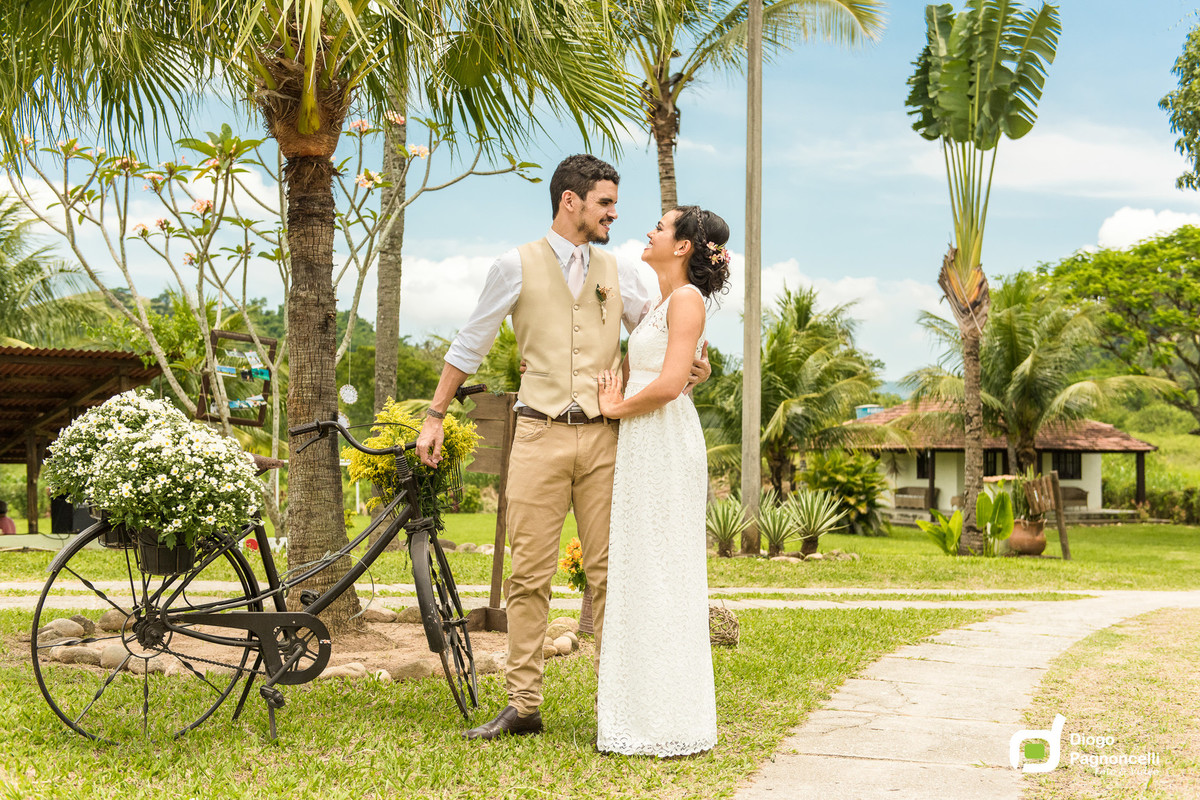 Noivos apaixonado se olhando no caminho da fazenda com jarros de flores e bicicleta antiga ao fundo. Foto Diogo Pagnoncelli.