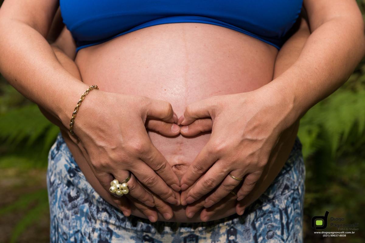 Detalhe da barriga da gestante com marido e ela fazendo o simbolo do coração com as mãos. Foto Diogo Pagnoncelli.