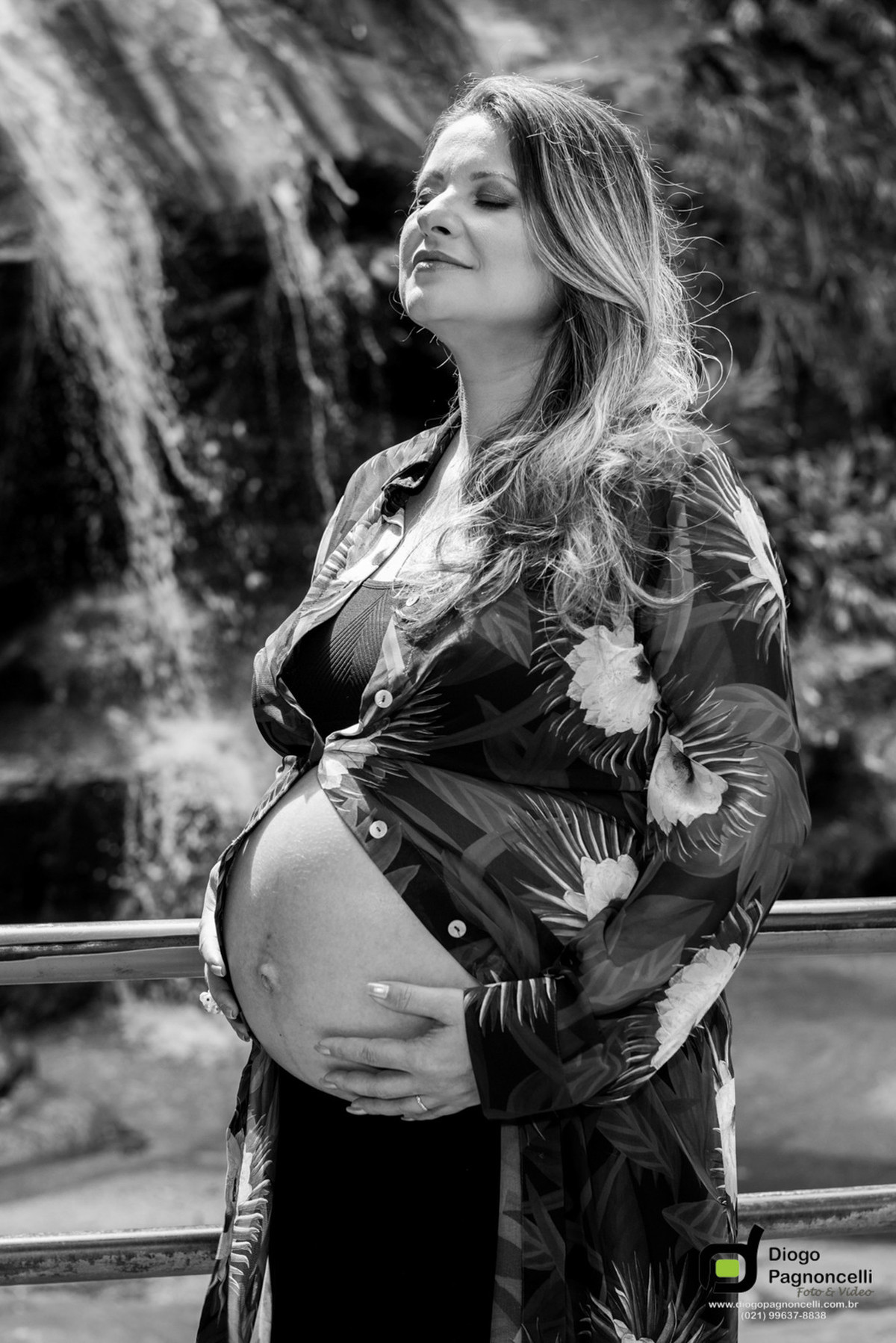Gestante de olhos fechados com as mãos na barriga com cachoeira de fundo em preto e branco. Foto Diogo Pagnoncelli.