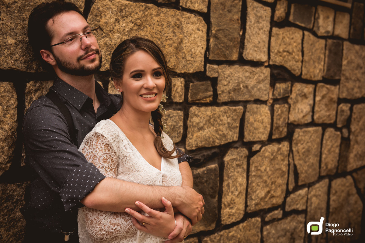 Noivos abracados encostados em uma parede de pedras. Foto Diogo Pagnoncelli.