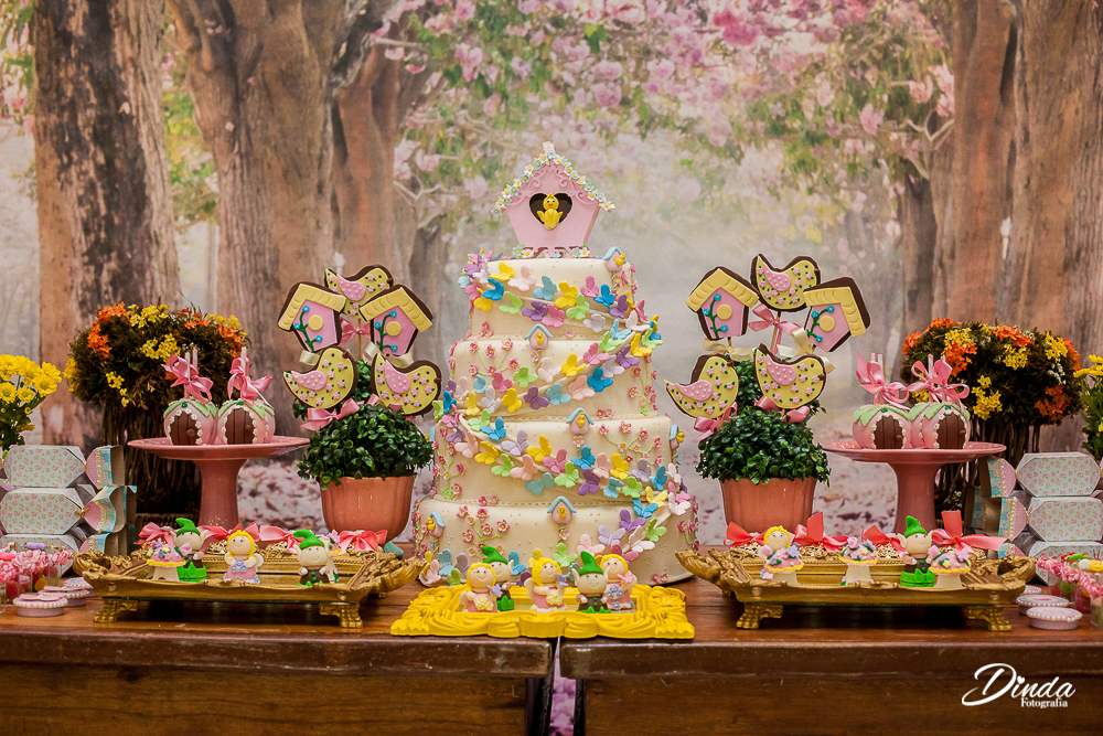 mesa de decoração com tema jardim encantado, duendes, flores, borboletas e passaram completam o cenário.