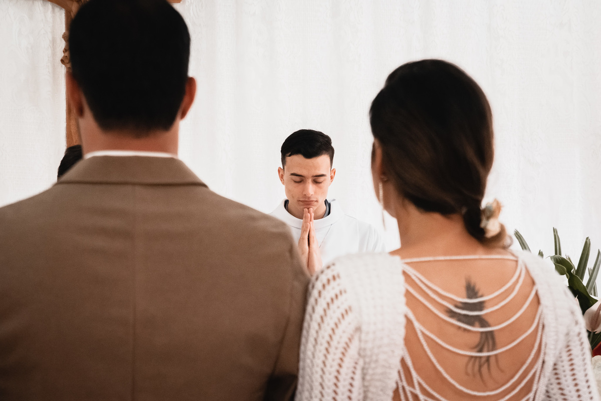Fotografo de Casamento em Valença - RJ. Casamento em Rio Preto Minas Gerais. Foto dos noivos de costas e o padre, irmão da noiva, aparece entre eles
