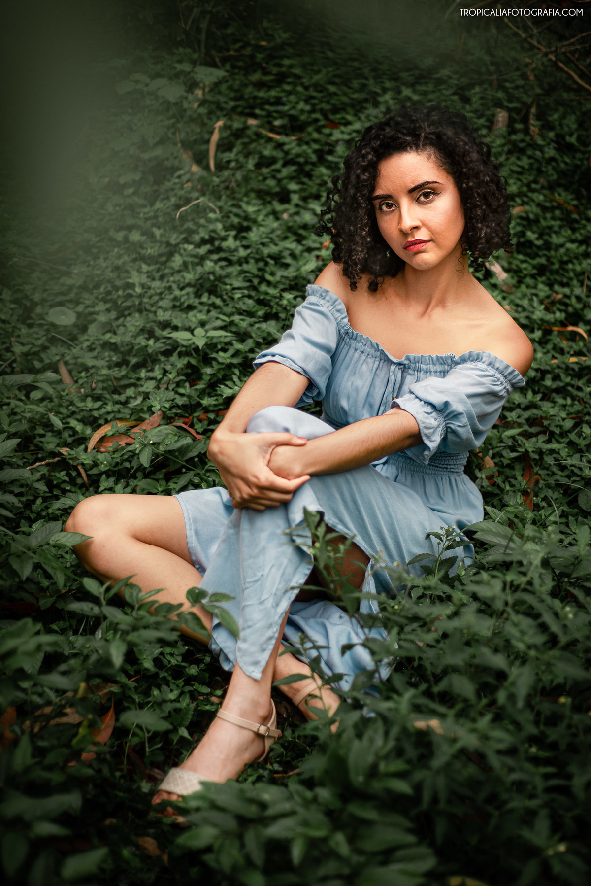 Fotógrafo em Nova Friburgo Ensaio Feminino, foto da mulher  sentada na grama com as mãos envolvendo um dos joelhos