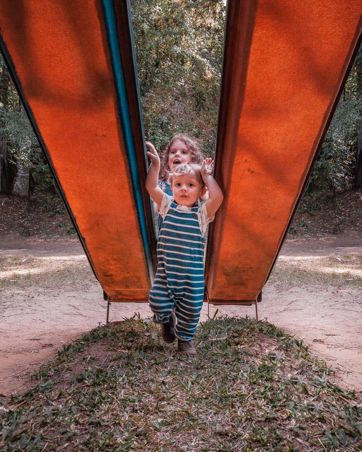 Ensaio externo documental de família em Nova Friburgo, foto das crianças passando entre dois escorregadores