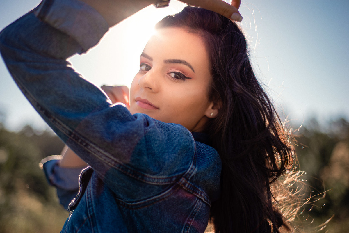 Ensaio feminino de 15 anos em Nova Friburgo, foto da menina mexendo nos cabelos com a luz do sol no fundo