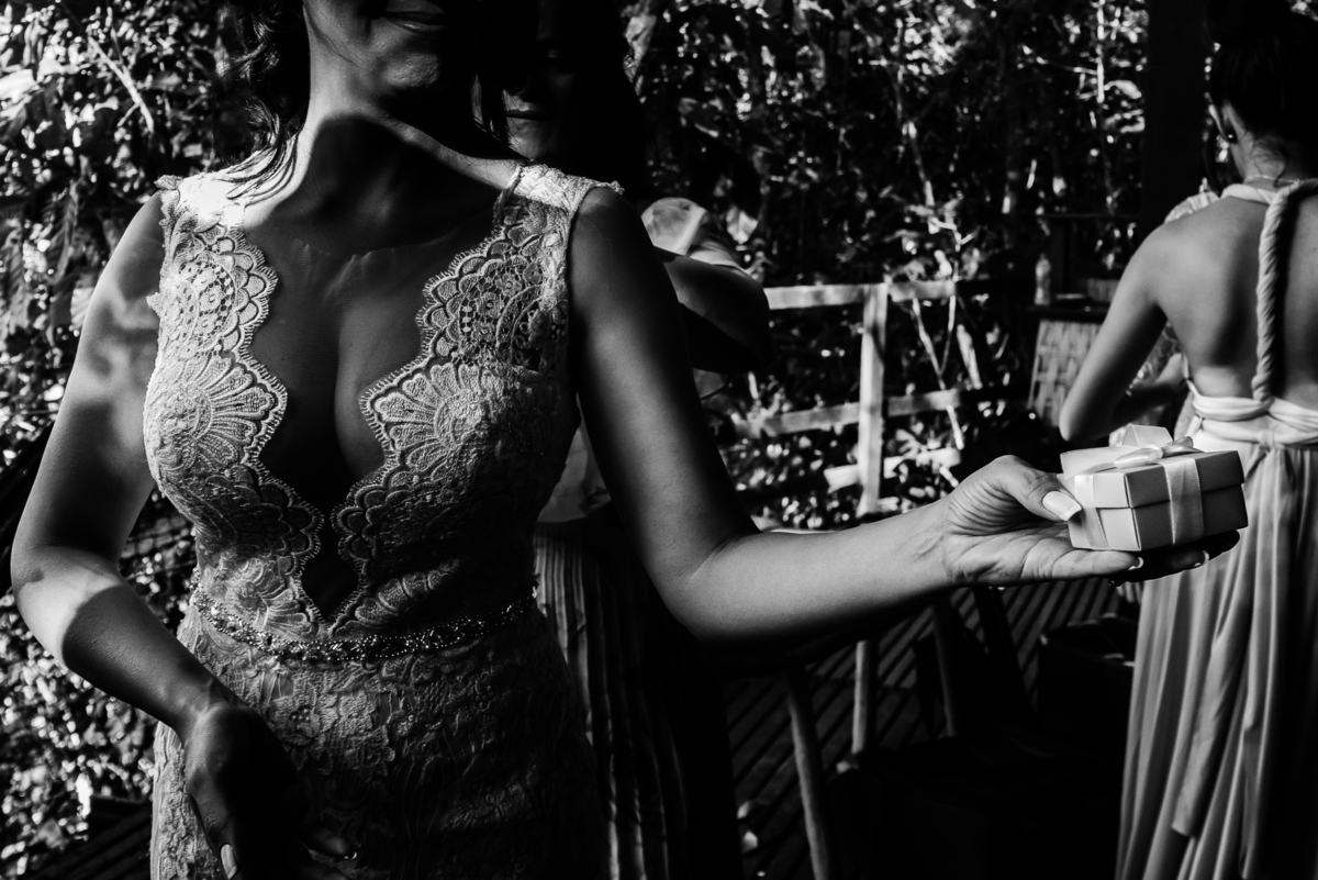 Fotografo de Casamento em Nova Friburgo - RJ. Destination Wedding em Paraty Mirim. Foto em preto e branco da noiva segurando uma caixinha de presente enquanto sua mãe fecha seu vestido