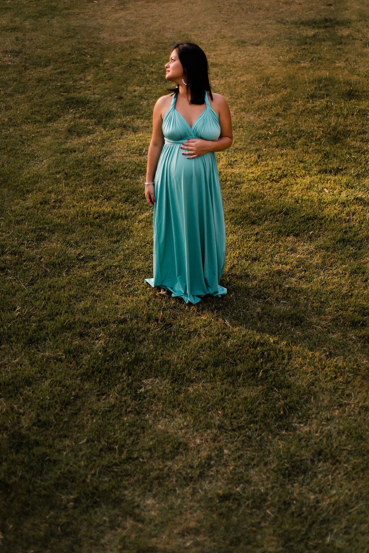 Ensaio externo de gestante em Nova Friburgo, foto da gestante caminhando na grama com a mão na barriga