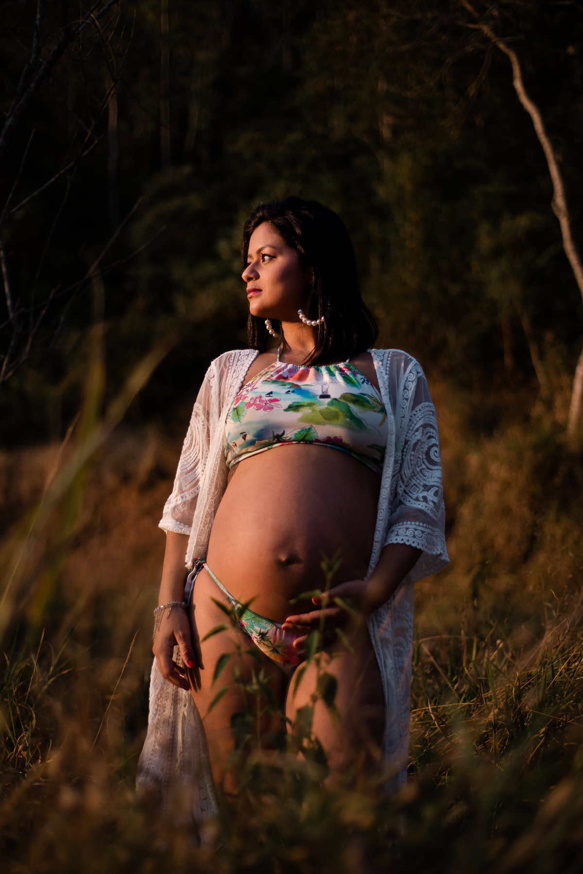 Ensaio externo de gestante em Nova Friburgo, foto da gestante em grama alta olhando para o horizonte com a mão na barriga