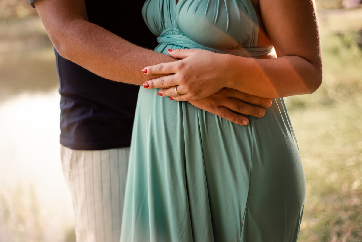 Ensaio externo de gestante em Nova Friburgo, foto de detalhe das mãos da gestante e do seu companheiro na barriga