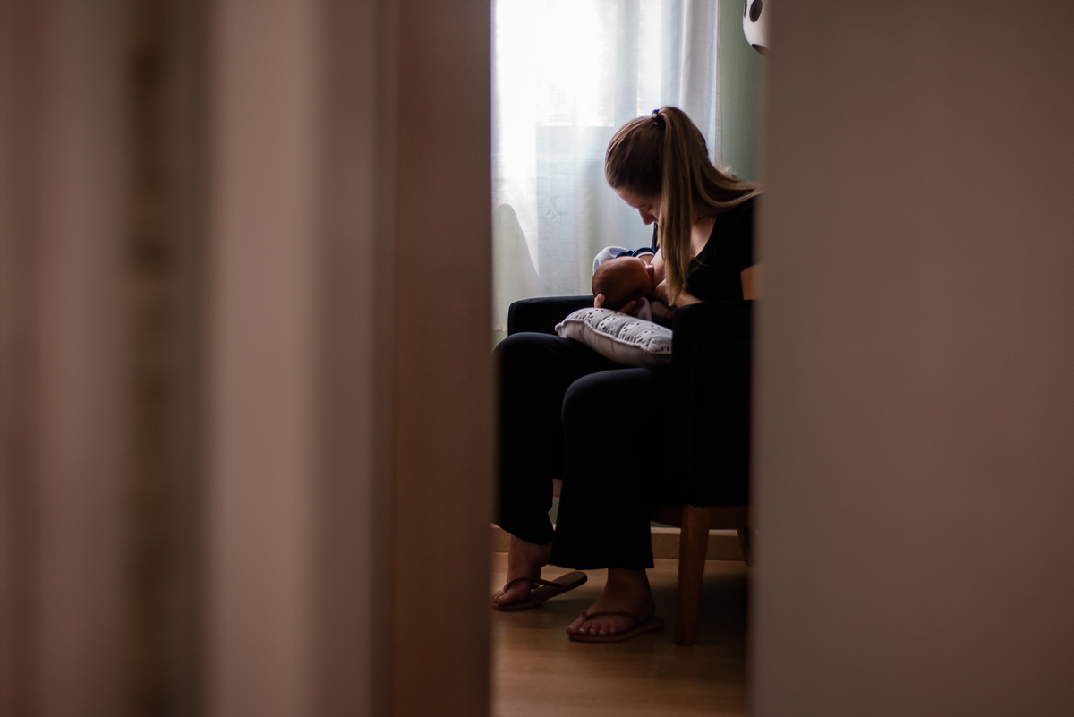 Ensaio de gestante e família em Nova Friburgo. Foto da mãe sentada em um cadeirão amamentando o filho recém nascido