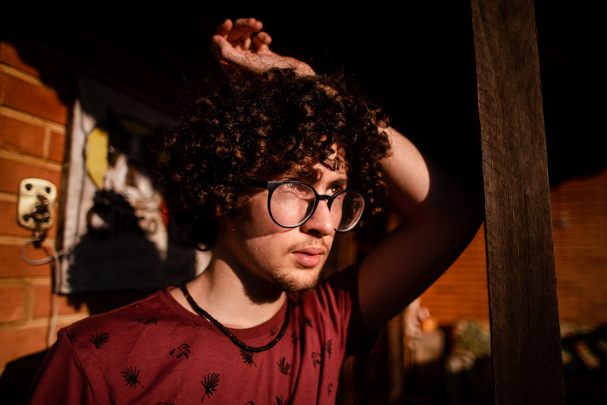 Fotógrafo em Nova Friburgo Ensaio Masculino, foto do menino olhando para o horizonte, apoiado em uma coluna de madeira