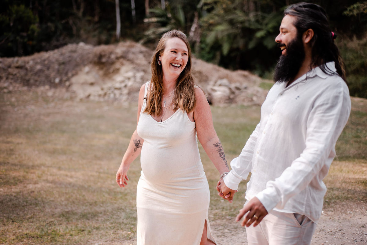 Ensaio externo de gestante em Nova Friburgo, foto da gestante sorrindo de mãos dadas com o companheiro