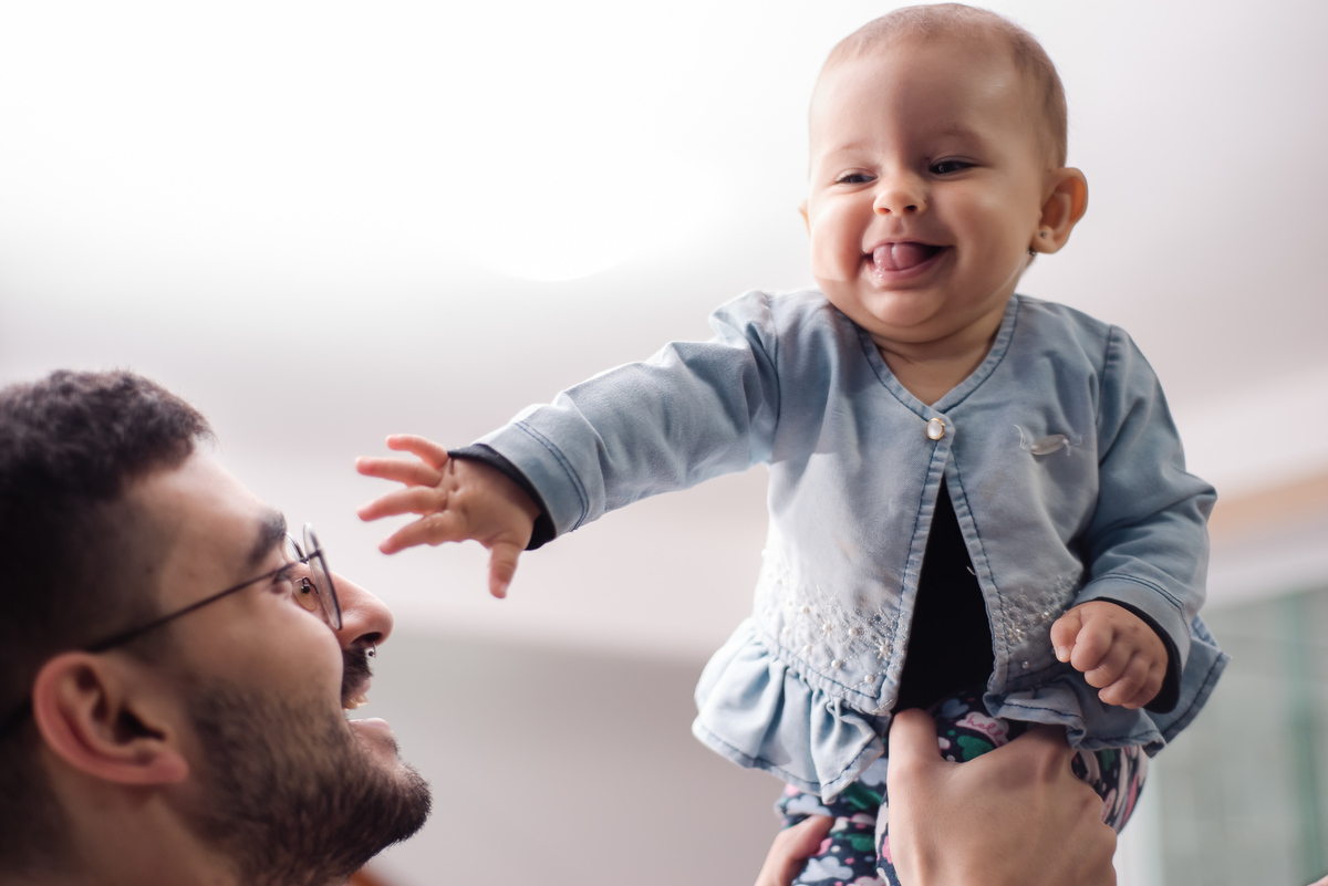 Ensaio documental de família com a Laura em casa. Foto do pai levantando a filha e sorrindo
