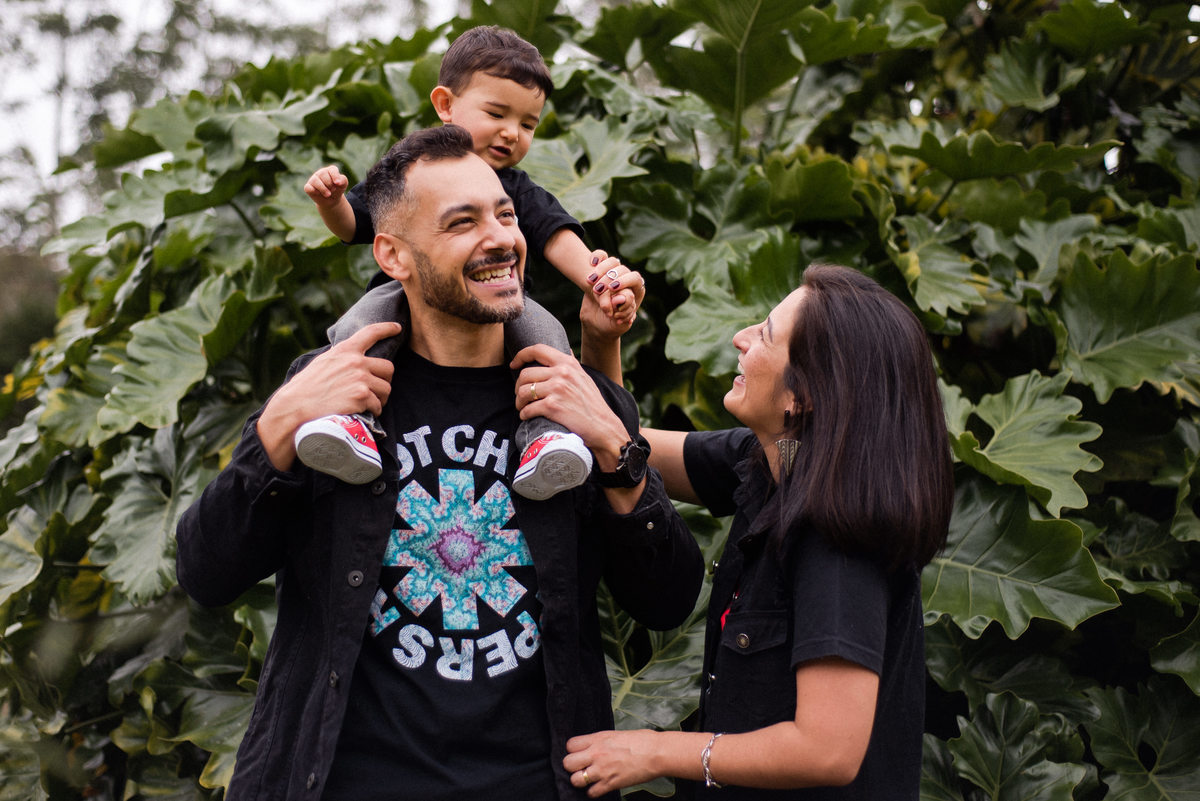Ensaio externo documental de família em Nova Friburgo, Região Serrana do Rio de Janeiro. Foto da criança sentada nos ombros do pai e brincando com a mãe