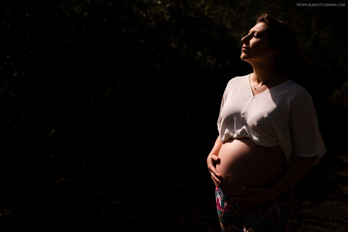 ensaio gestante em nova friburgo, região serrana do rio de janeiro no hotel oberland. Foto da gestante iluminada pelo sol em um fundo preto