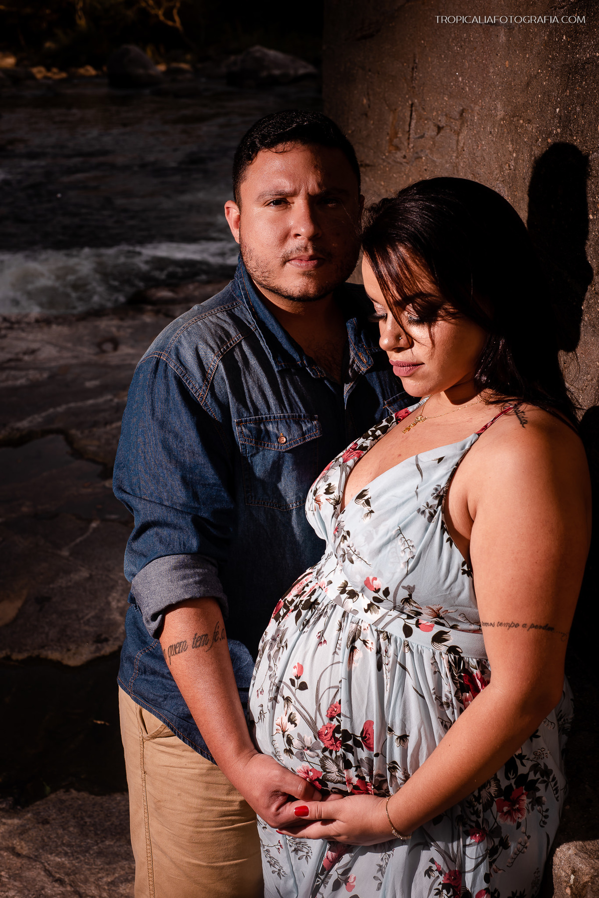 ensaio externo de gestante na cachoeira encontro dos rios em nova friburgo, região serrana do rio de janeiro. Foto da gestante e do companheiro olhando para a barriga 