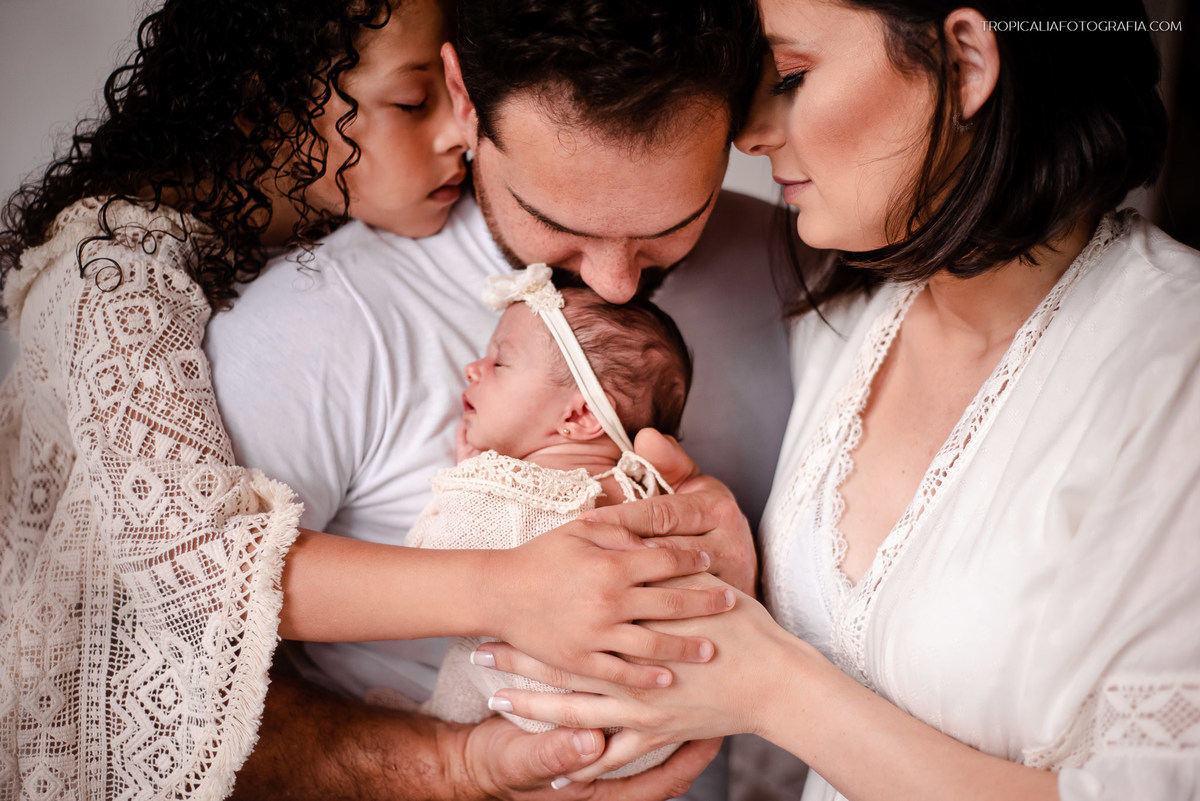 Ensaio documental de família em casa feito por fotógrafos em nova friburgo região serrana do rio de janeiro. Foto da família abraçada reunida em volta da bebê recém nascida