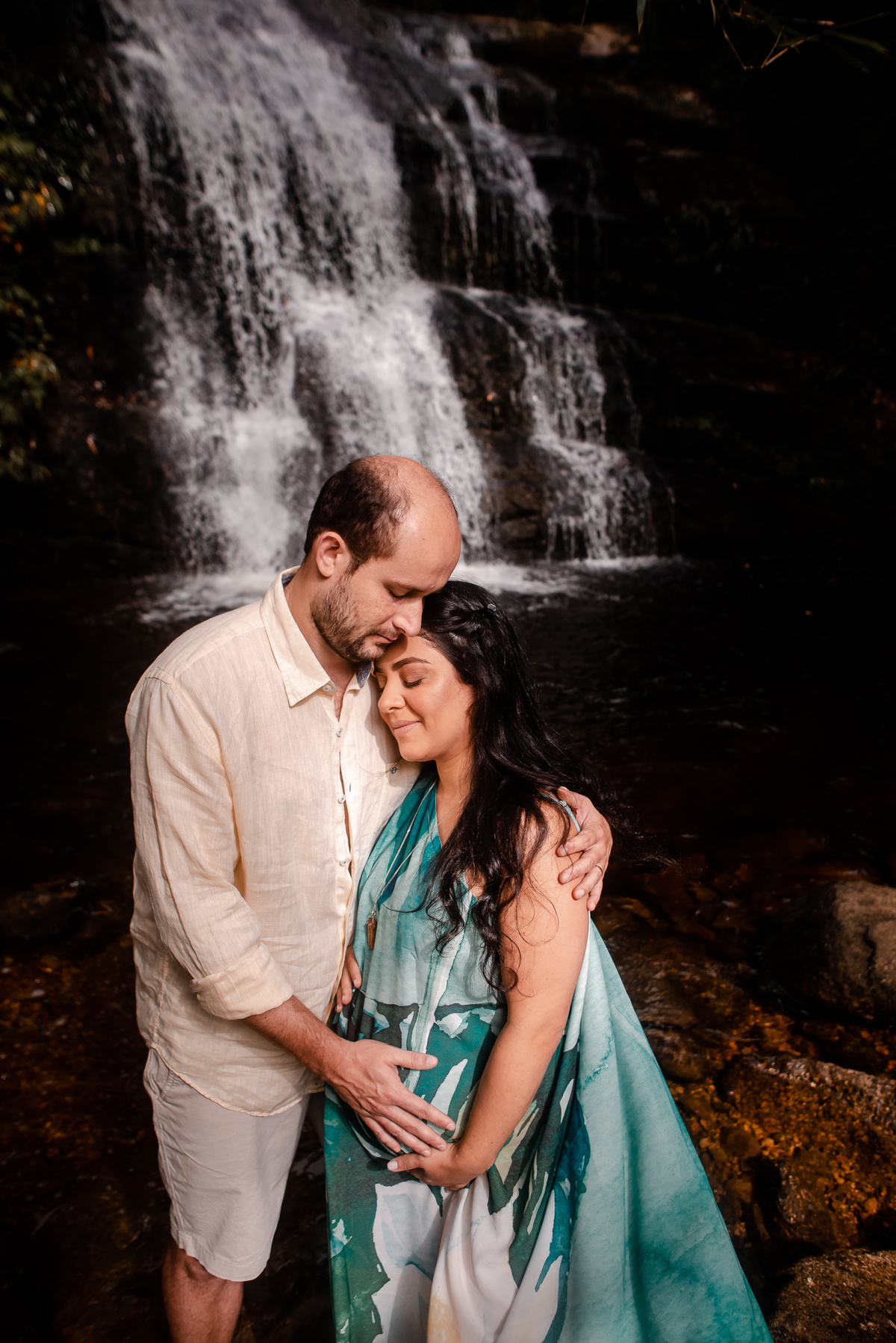 ensaio externo de gestante na cachoeira em nova friburgo, região serrana do rio de janeiro. Foto da gestante e o companheiro abraçados de olhos fechados