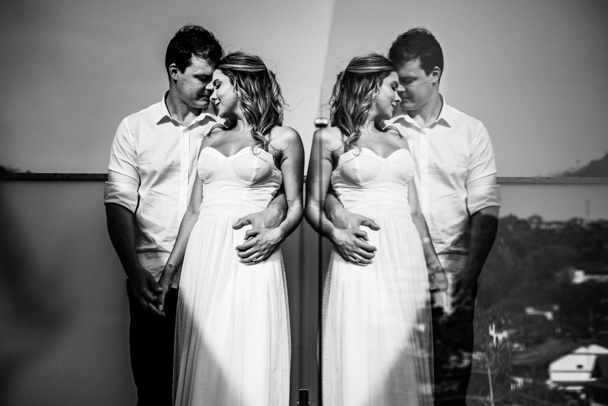 Fotógrafo de casamento em Nova Friburgo. Ensaio pré wedding do casal.  Foto em preto e branco dos noivos abraçados e o seu reflexo aparecendo em um vidro ao lado