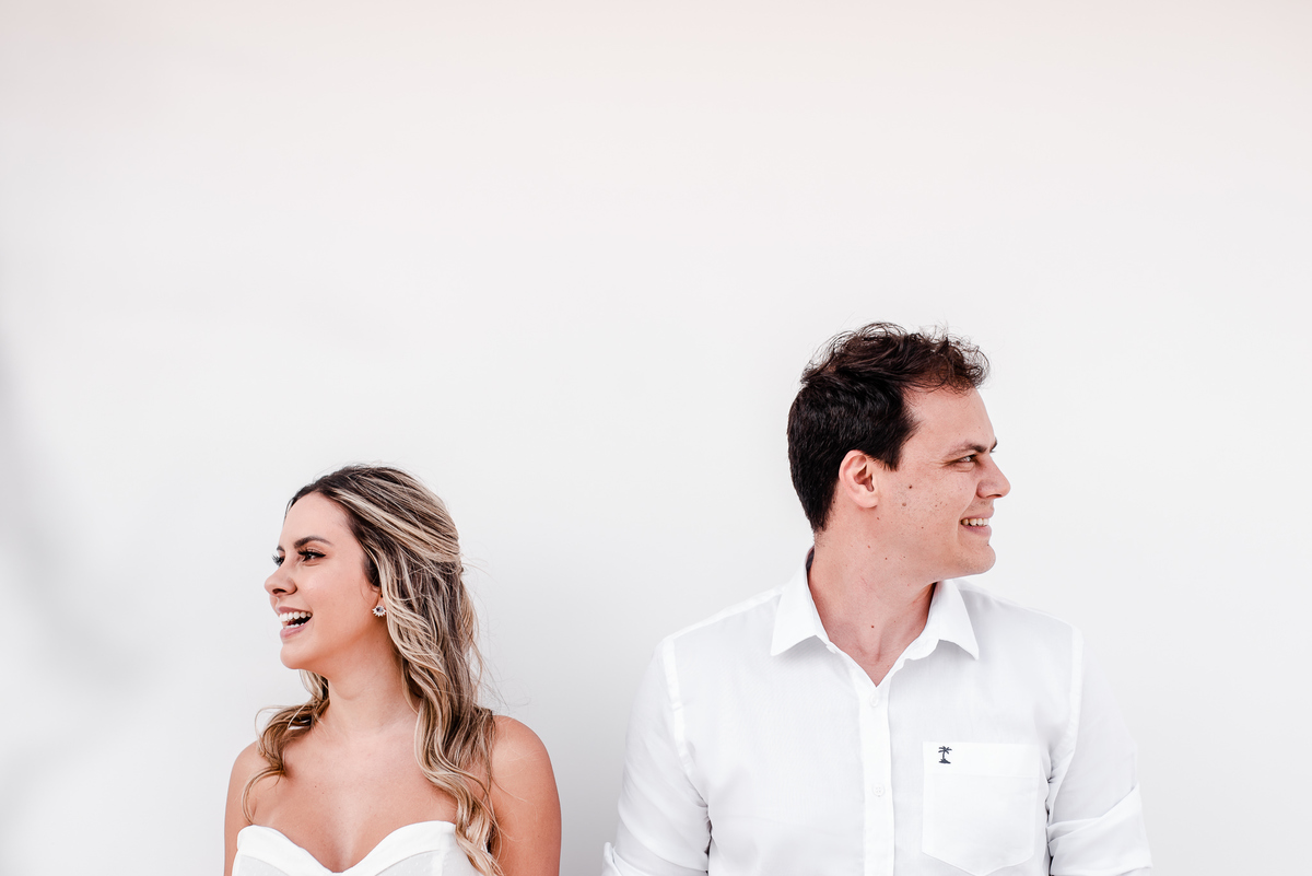 Fotógrafo de casamento em Nova Friburgo. Ensaio pré wedding do casal.  Foto dos noivos de mãos dadas em frente a uma parede branca olhando para lados opostos