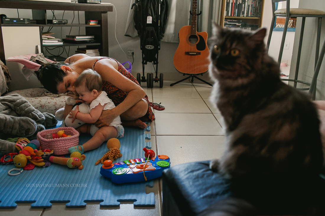 Mamãe brincando com sua filha e gato olhando.