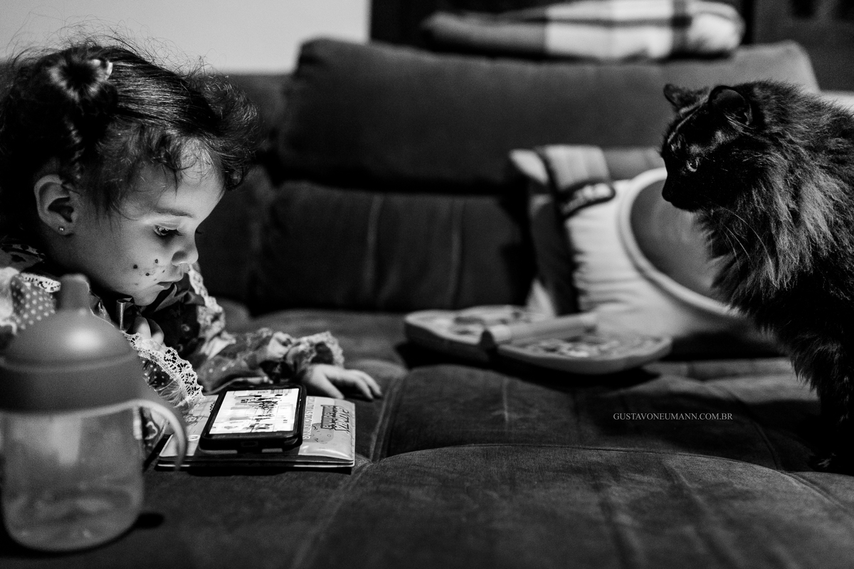 Criança brincando no celular com gatinho olhando