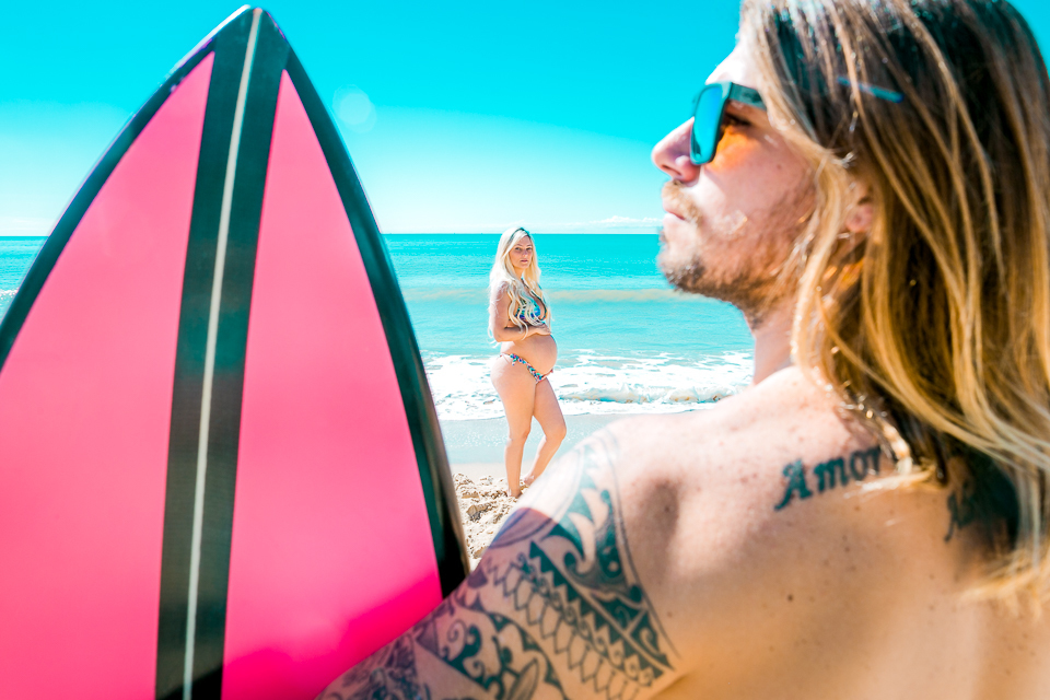 Gestante na foto com o marido curtindo o sol e sua prancha
