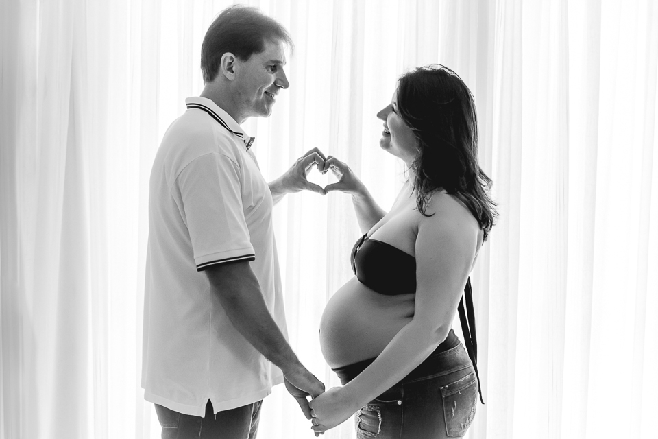 Casal fazendo coração, num gesto de amor no ensaio gestante. 