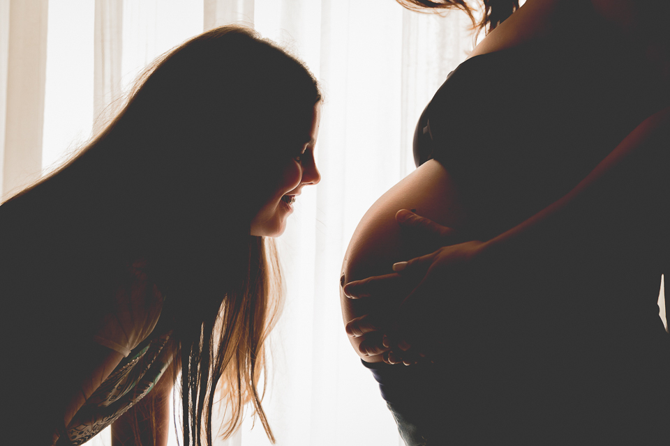 Foto da irmã dando um carinho na barriga na mãe grávida. 