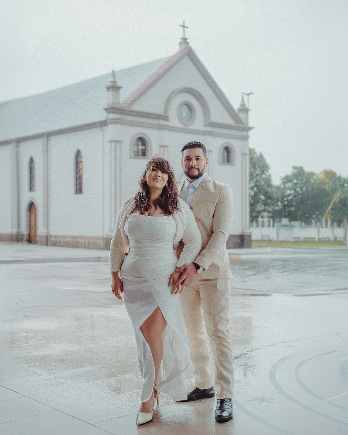 Ensaio fotográfico de casal recém-casado em frente a uma igreja no santuário de Caravaggio, com os noivos de mãos dadas e vestidos para a cerimônia.