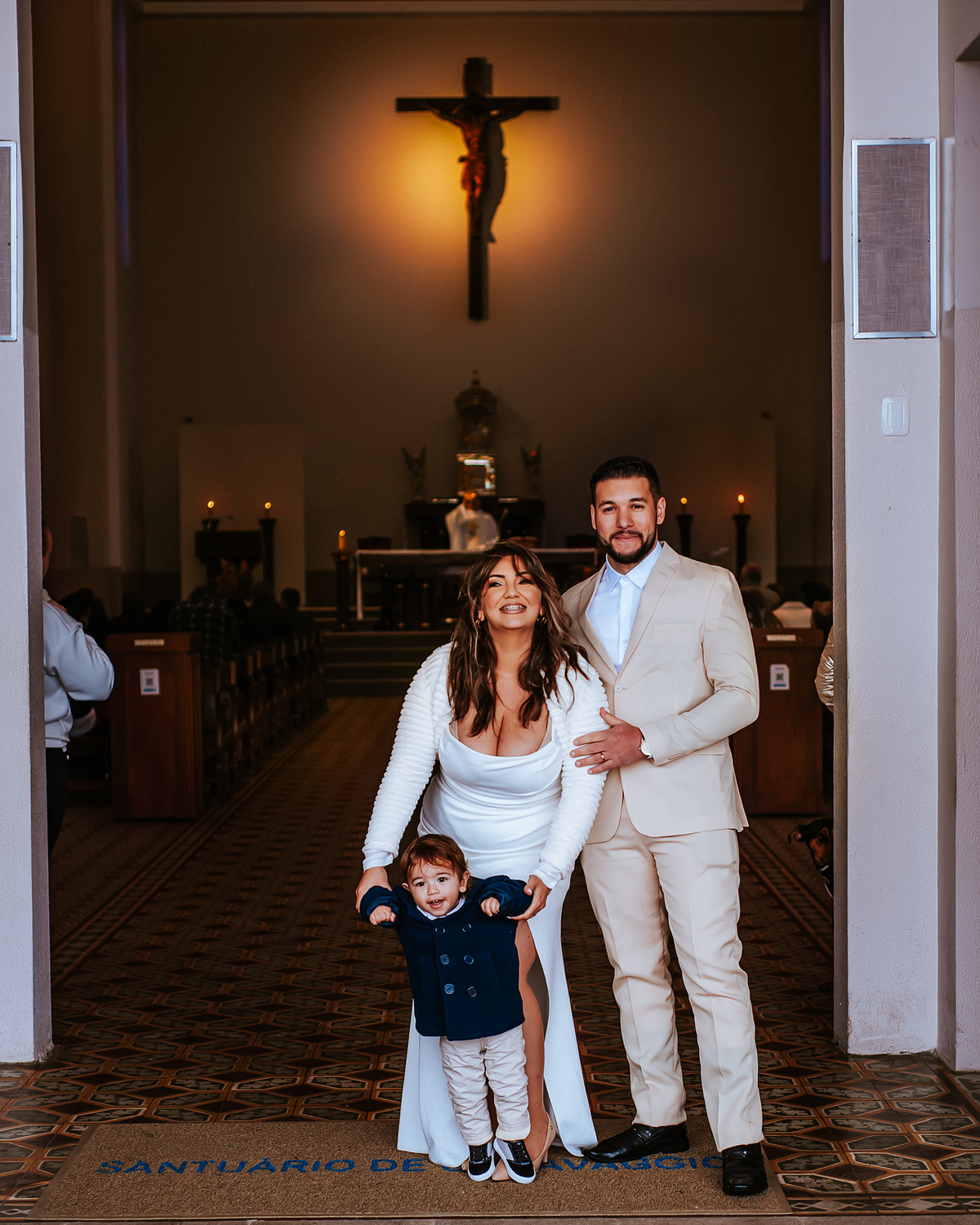 Casal recém-casado fotografado na entrada do santuário de caravaggio em Farroupilha, com o altar e o crucifixo ao fundo.