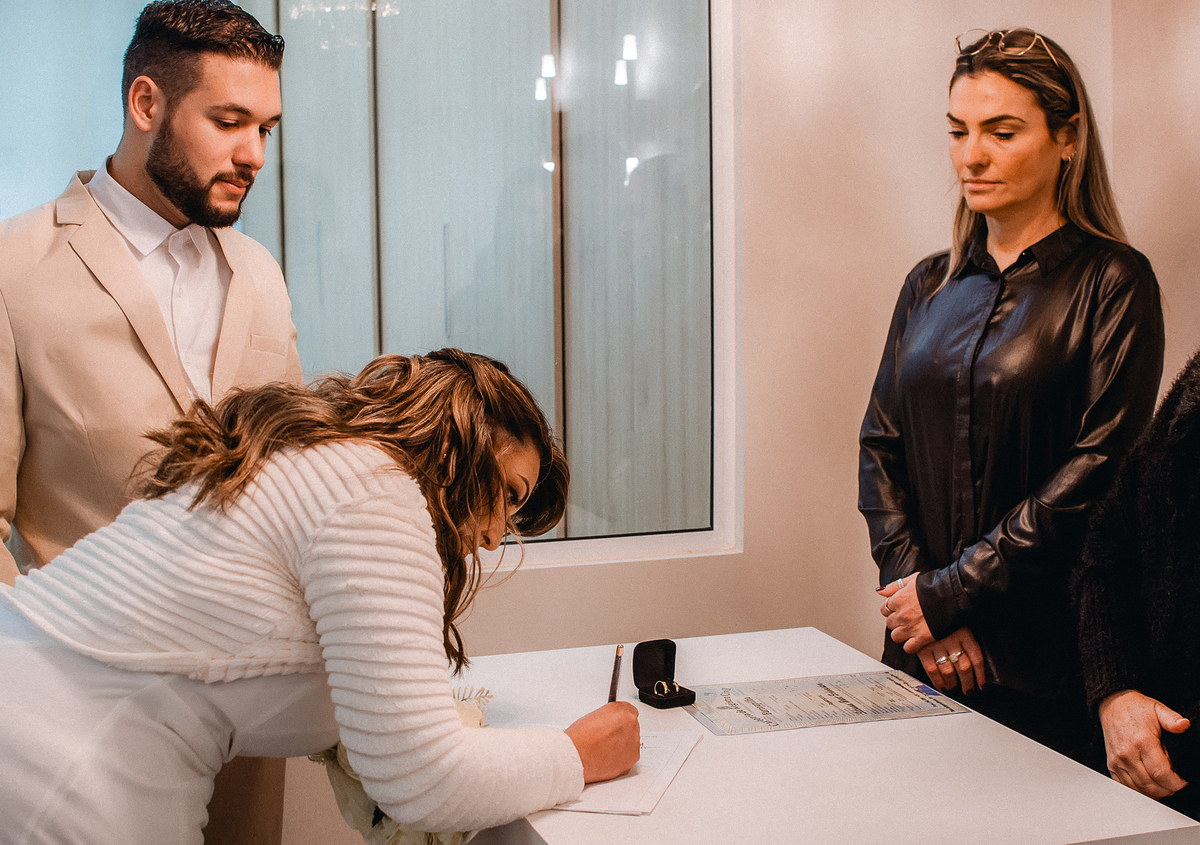Noiva assina o registro de casamento civil em Farroupilha, RS, enquanto o noivo e as testemunhas acompanham a cerimônia.