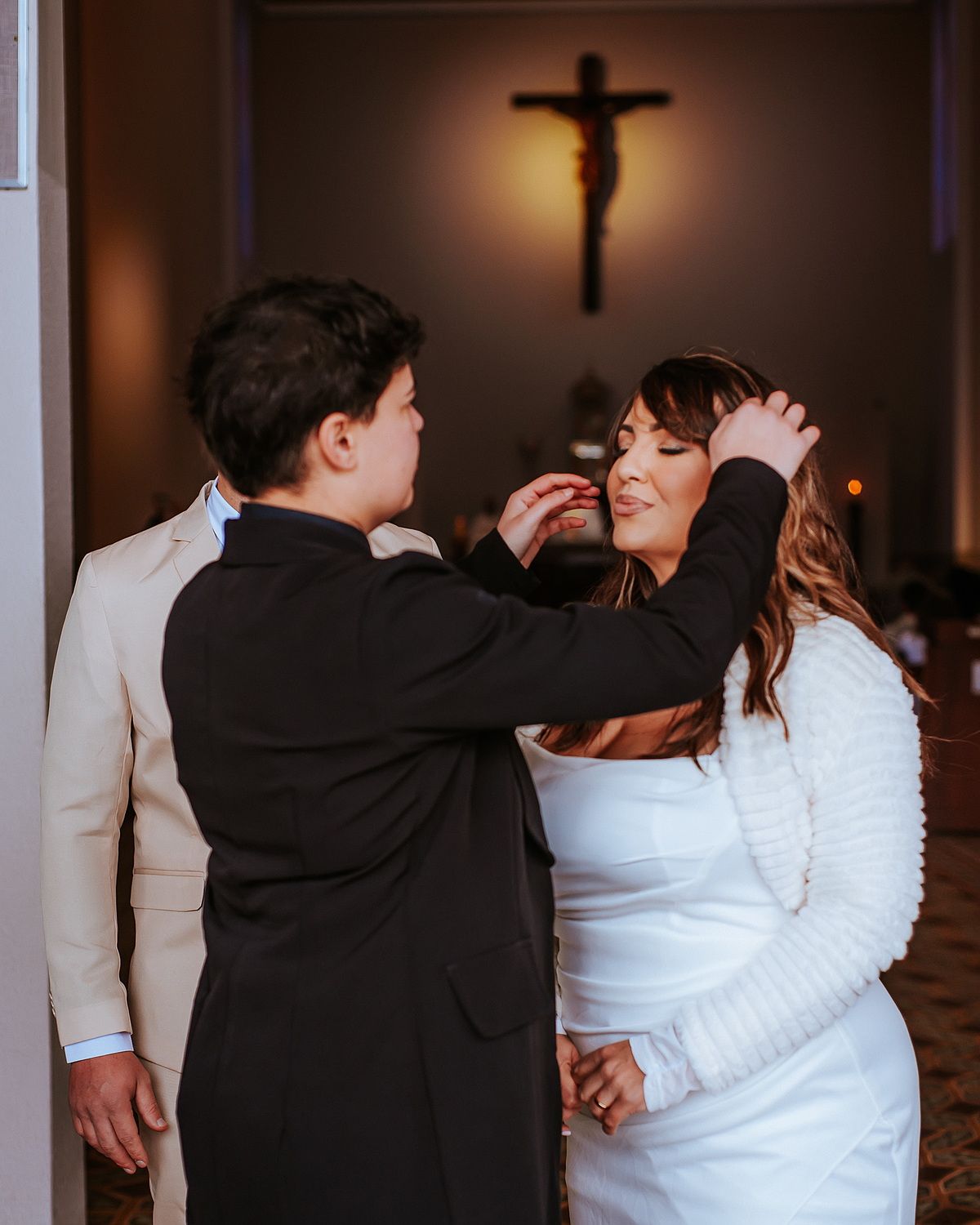 Criança ajeita delicadamente o cabelo da noiva durante os registros fotográficos de casamento no interior de uma igreja.