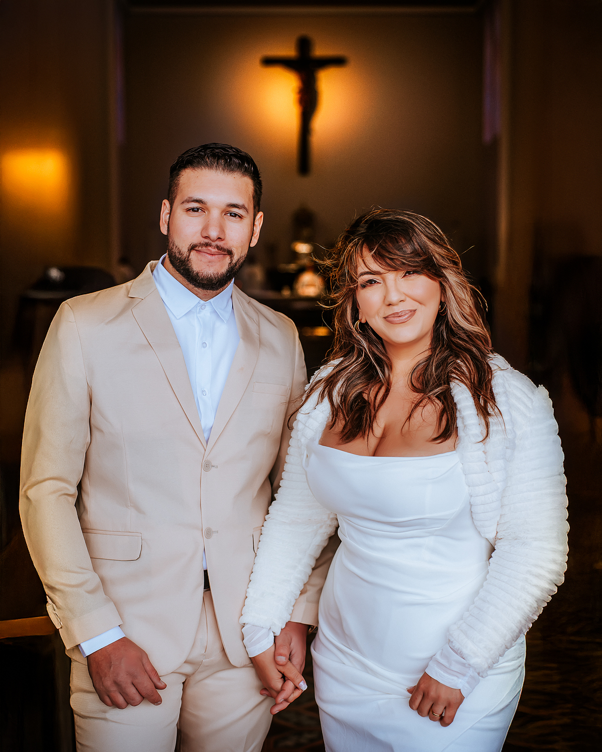 etrato dos noivos juntos no interior de uma igreja, com traje claro e vestido branco, após a cerimônia de casamento.